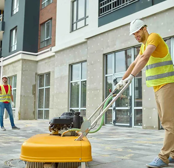 Professional using a walk-behind floor cleaning machine outside a modern building in Grand Rapids MI.