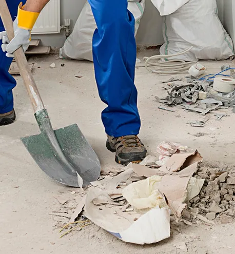 Worker shoveling debris and dust into a pile during final construction cleaning.