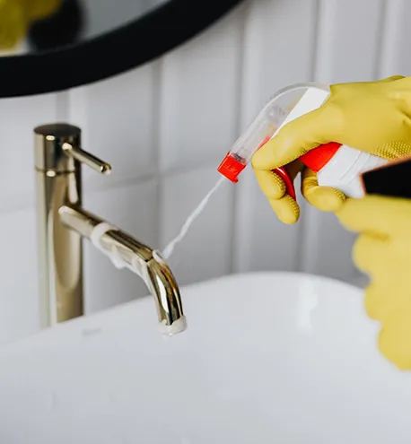 Close-up of hands in gloves cleaning a faucet with cleaning products.