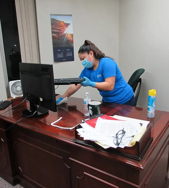 Cleaning professional disinfecting a desk in a corporate office in Ann Arbor MI.